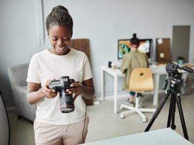 Portrait of smiling African American woman holding camera while working in photo studio, copy space